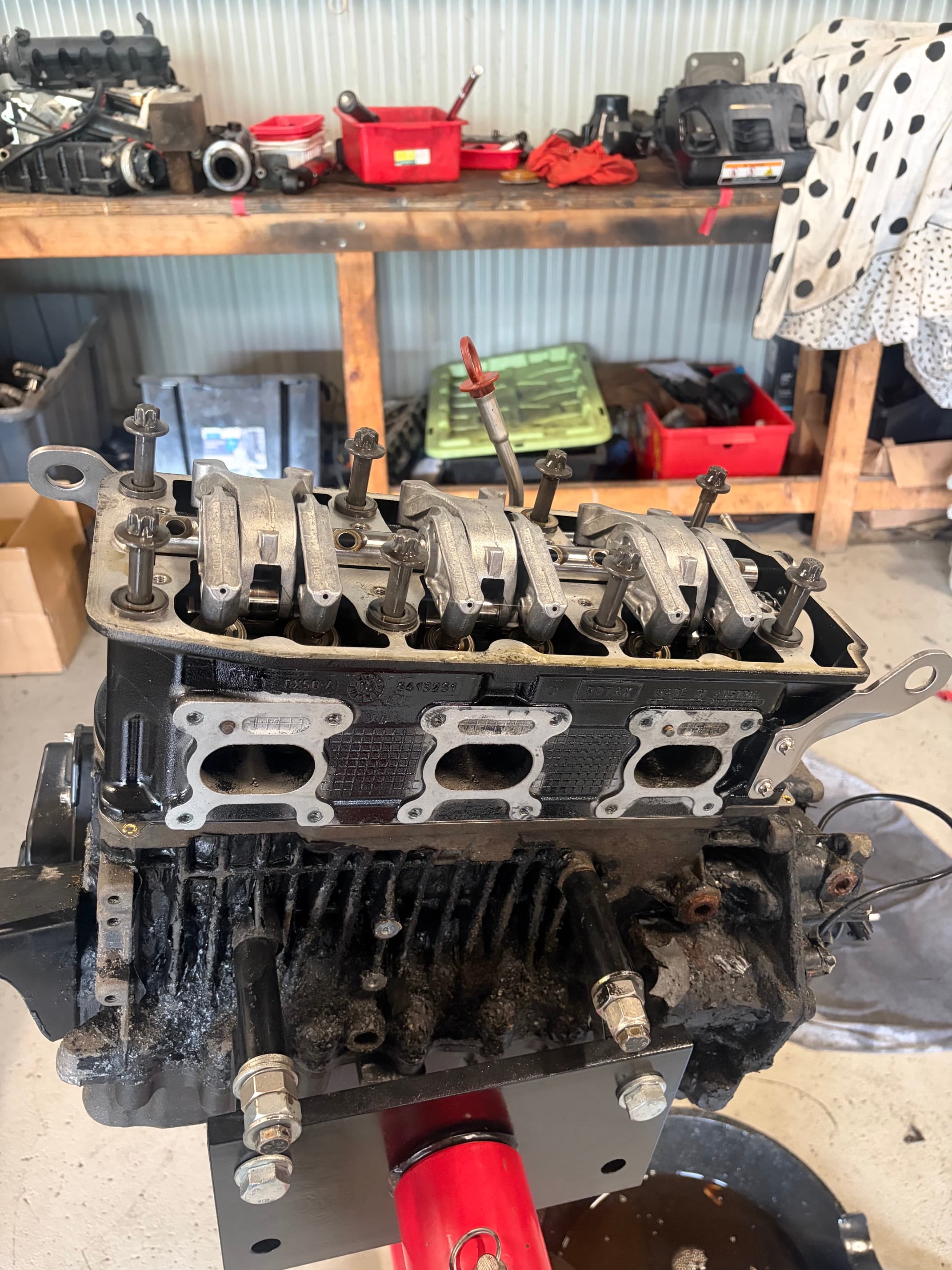 A partially disassembled three-cylinder engine with exposed rocker arms mounted on a red stand.