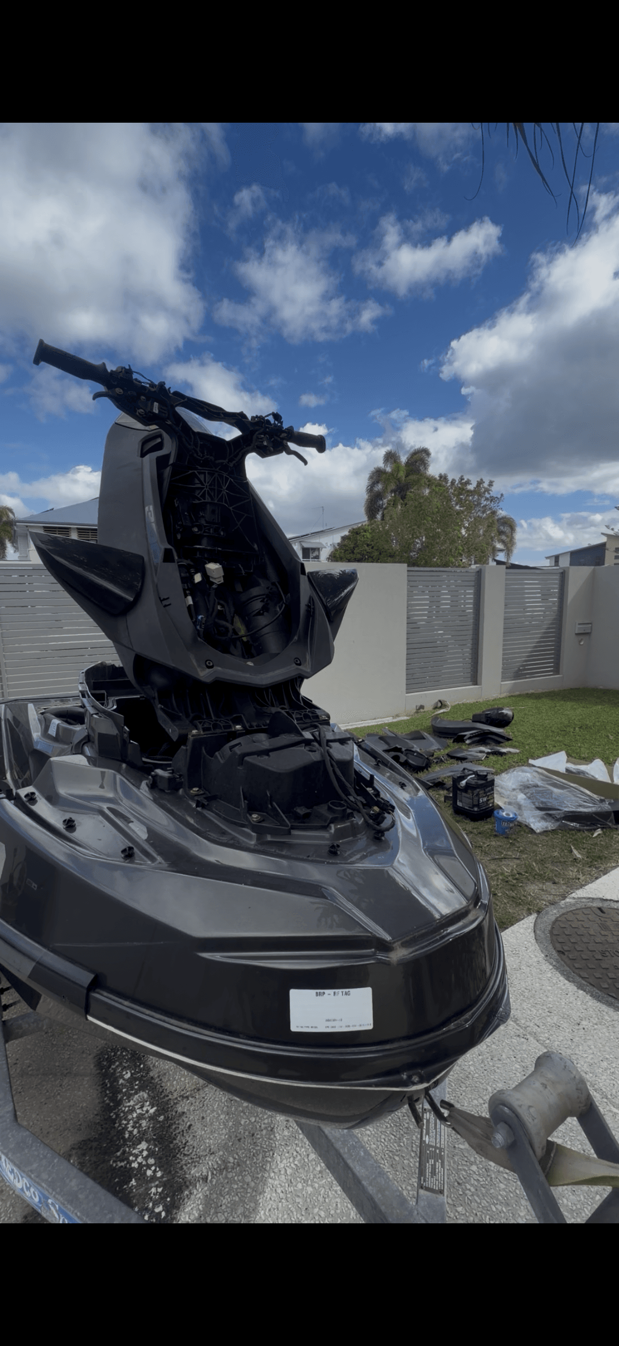 Partially disassembled black jet ski on a trailer with internal components and steering assembly exposed.